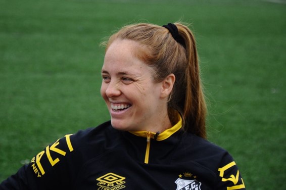 Jogadora Ketlen Wiggers sentada em frente ao gramado sorrindo durante a entrevista da Agenzia.