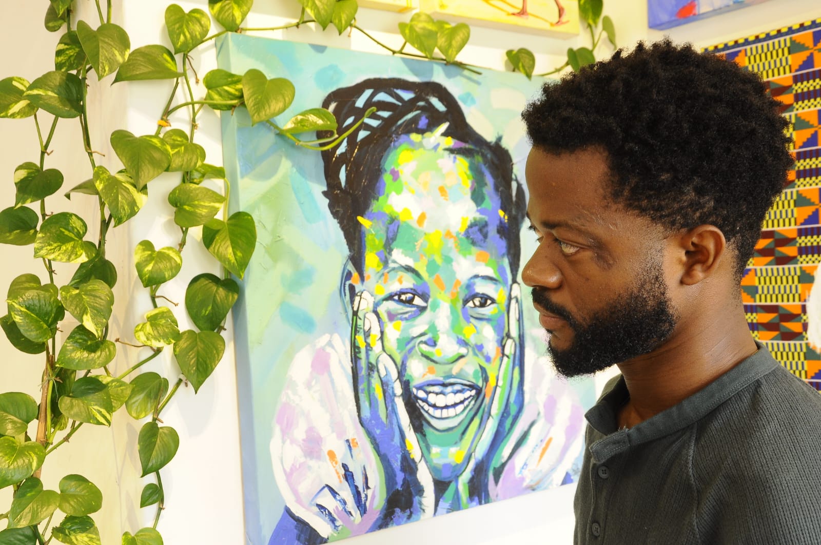 Paulo Chavonga de perfil olhando para uma de suas pinturas, o artista é negro e utiliza uma blusa de manga longa cinza, o rosto possui barba e o cabelo é crespo.

A pintura pendurada na parede é de uma criança do sexo feminino sorrindo, a criança possui traços negros apesar da pintura ter sido colorida apenas com pontos em verde, laranja, azul, amarelo e lilás, o preto apenas foi utilizado nas tranças do cabelo. Na parede, algumas vinhas de planta sobem e criam uma moldura natural para a pintura.