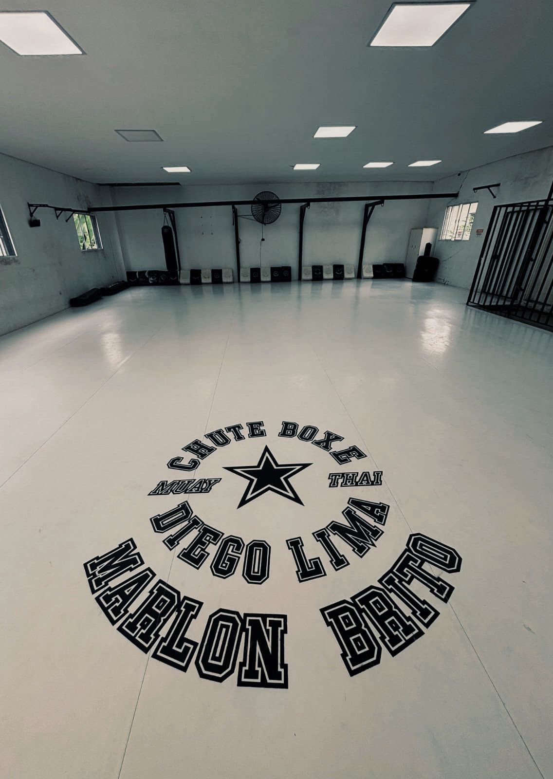 Visão geral do tatame de treino com a logomarca da academia Chute Boxe estampada no piso.