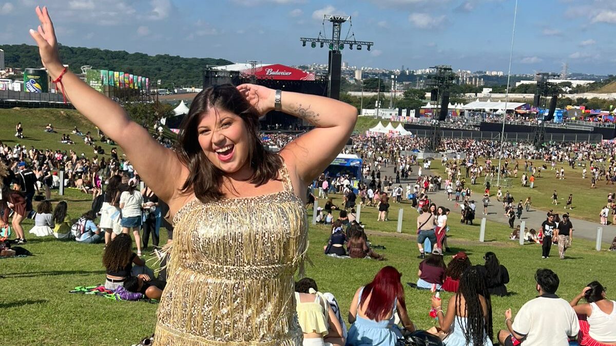 Mulher, com vestido dourado de franjas, faz pose levantando os braços para cima. Ela está presente no festival de música Lollapalooza. 