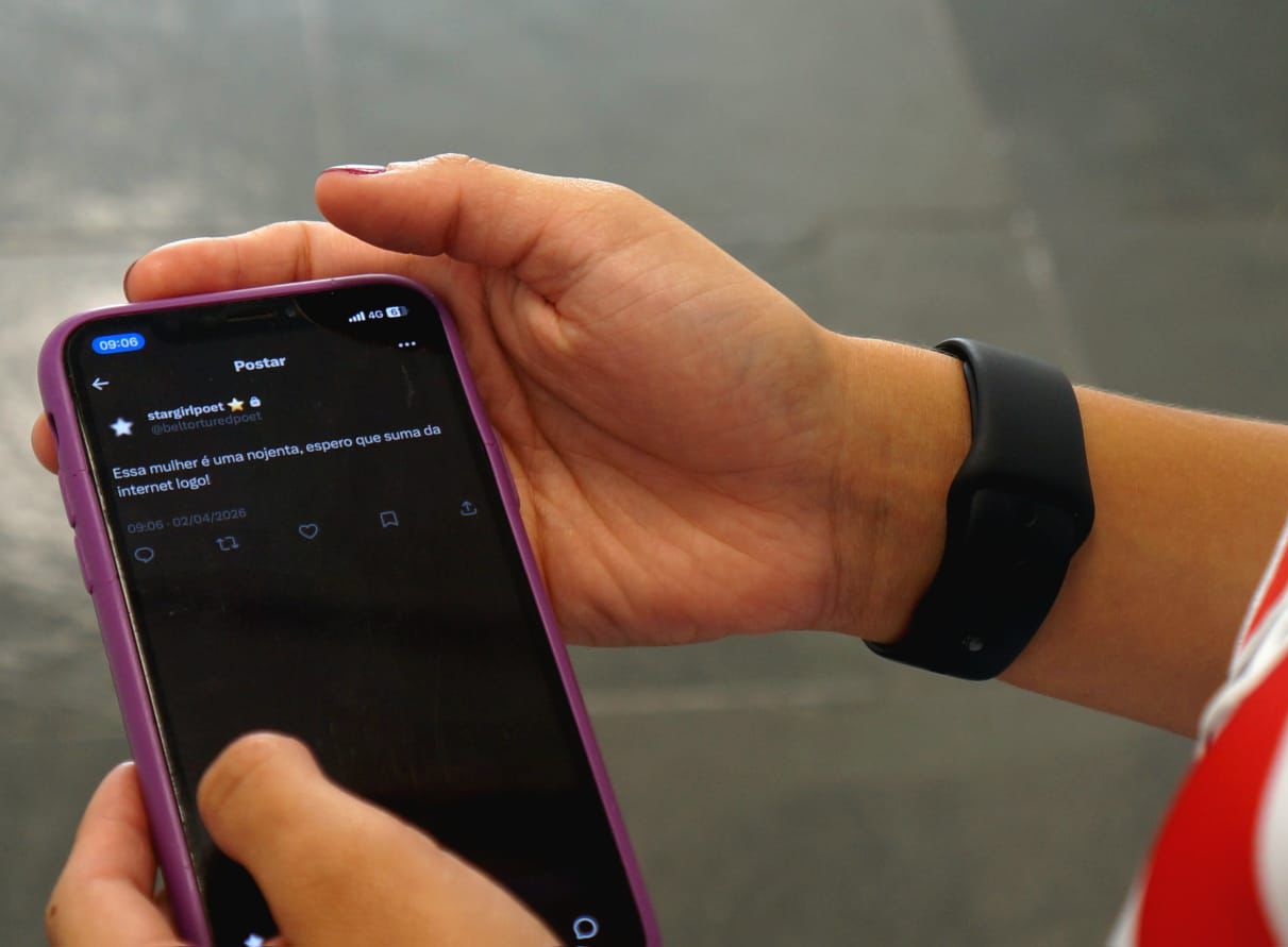 uma mão segurando um celular aberto no aplicativo X, com discurso de ódio