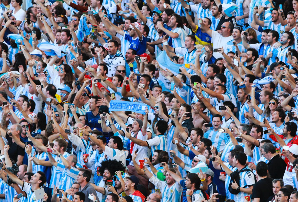 Torcedores da seleção de futebol da Argentina celebram e lotam uma arquibancada de estádio.